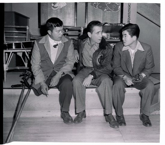 (Original Caption) Old friends meet again on the set of Tokyo Joe as Humphrey Bogart chats with two Nisei GI's he met during a wartime entertainment tour of Italy. Frank Fujino (left) and Don Seki (right), who fought with the most-decorated outfit in World War II, the 442nd Infantry Regiment. Both have speaking parts in Bogart's new picture.